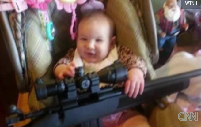 O imagine care a starnit controverse. Un bebelus a fost fotografiat de parinti cu o pusca in brate