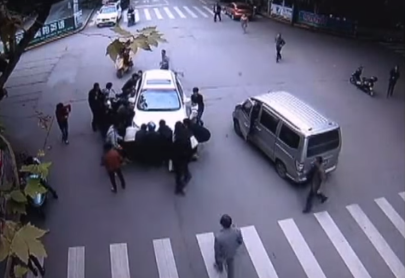 CAMERA DE SUPRAVEGHERE: O femeie este salvata de sub rotile unei masini de trecatori. Momentul in care ridica masina. VIDEO