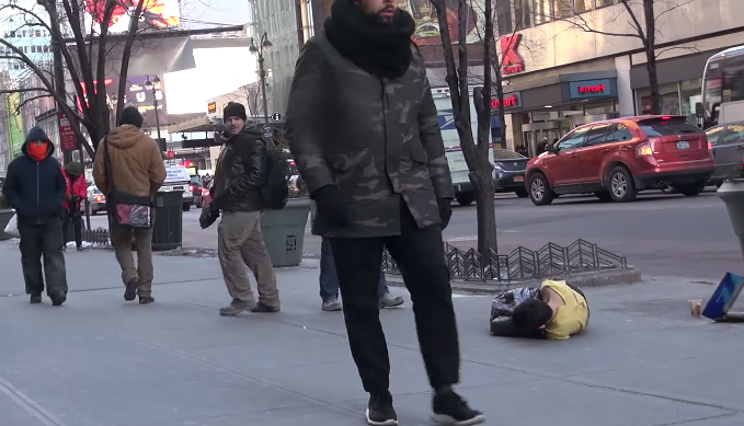 Un tanar tremura de frig pe asfalt, acoperit cu haine rupte si un sac de gunoi. Cum reactioneaza trecatorii la suferinta lui