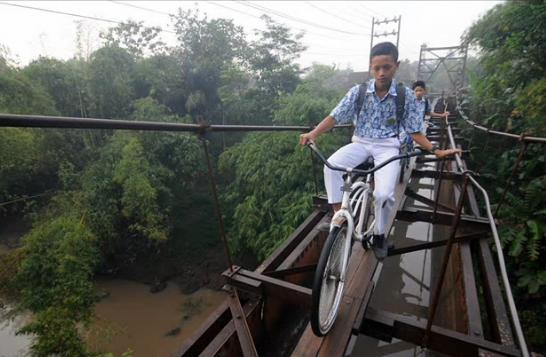 Cel mai periculos drum spre scoala: Copiii merg cu bicicleta pe scandurile de lemn ale unui pod suspendat