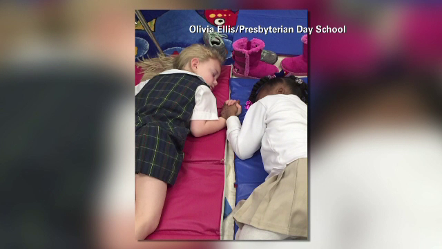 Doua eleve, una alba si cealalta de culoare, care se tin de mana in timp ce dorm. Dovada ca prietenia nu tine cont de rasa