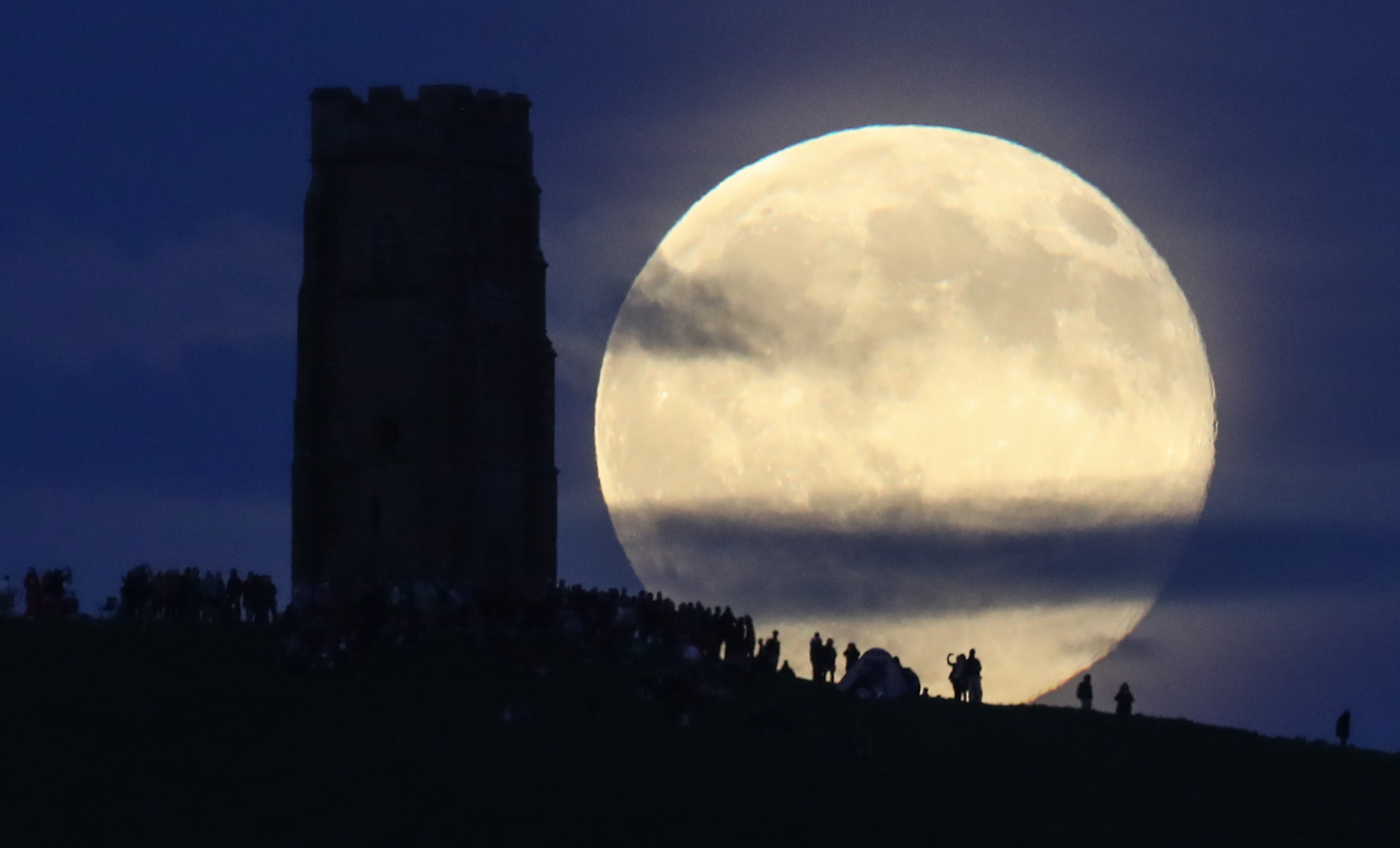 Luna plina, de culoare capsunei, deasupra Glastonbury Tor, la Solstitiul de vara