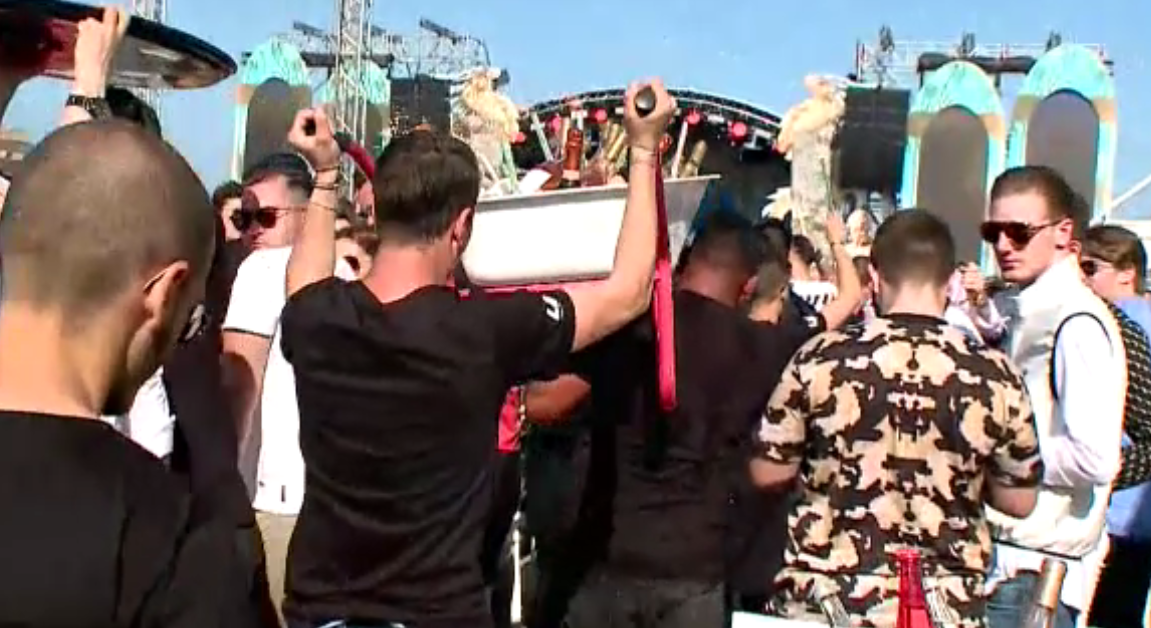 Momentul în care ospătarii duc o roabă cu vin la o masă, într-un club din Mamaia