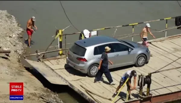 Un pod făcut prea scurt ruginește pe mal, în Maramureș. Oamenii trec Someșul cu un bac împins cu bețe